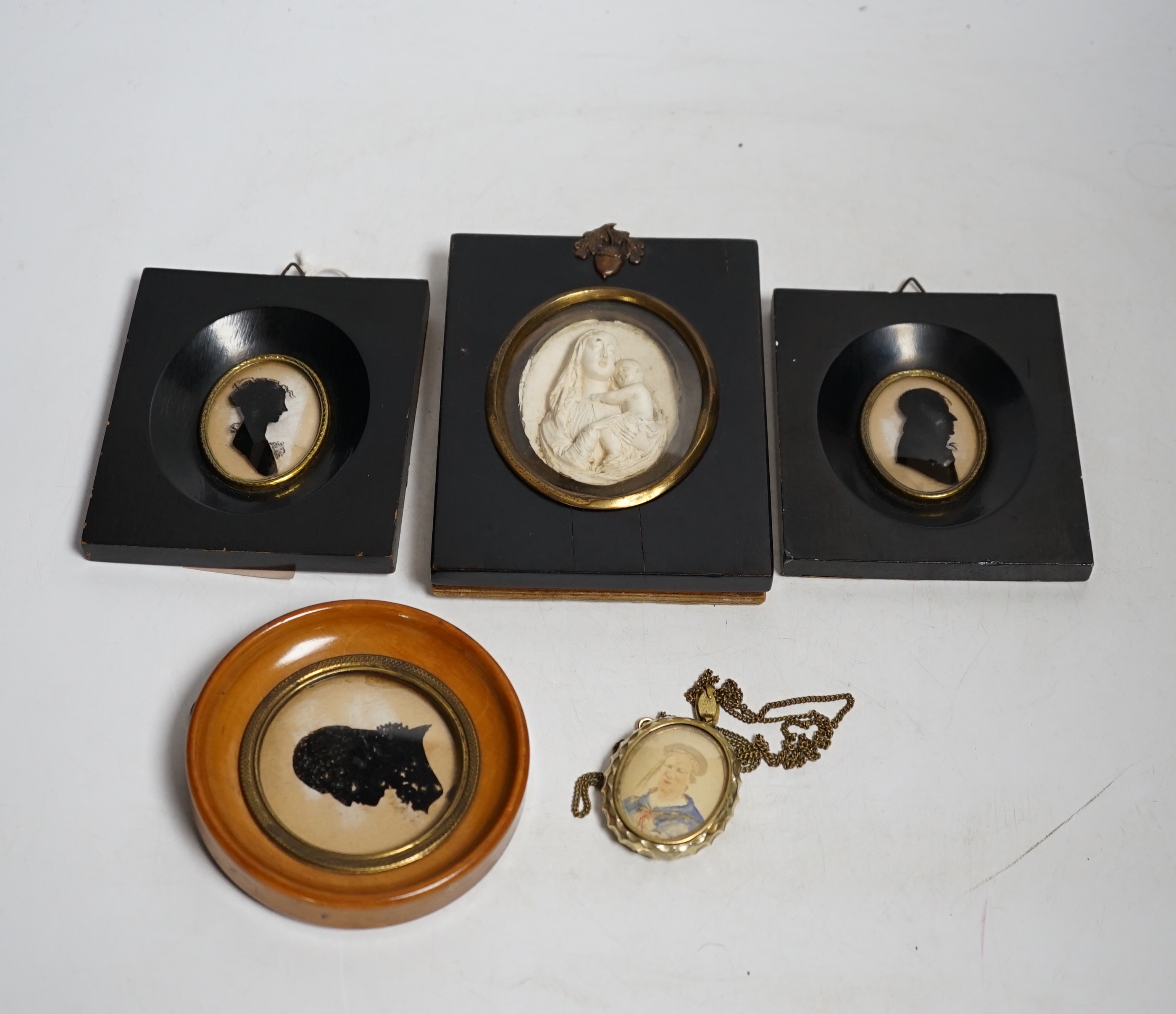 Three miniature reverse glass painted silhouettes, a relief plaque of the virgin and child and a watercolour portrait pendant